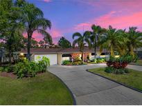 Charming home featuring tropical landscaping, a brick accent wall, and a spacious driveway leading to an attached garage at 650 Poinsettia Rd, Belleair, FL 33756