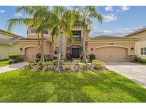 Elegant two-story home featuring a three-car garage, manicured lawn, and vibrant tropical landscaping at 2709 Coco Palm Cir, Wesley Chapel, FL 33543