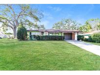 Charming single-story home with a well-manicured lawn and mature trees on a sunny day at 1453 Thames Ln, Clearwater, FL 33755