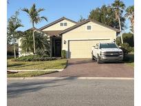 Charming single-story home with a two-car garage, brick driveway, landscaped yard, and palm trees at 1427 Hyssop Loop, North Port, FL 34289