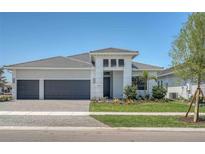 A modern, light gray, single-story home with a three-car garage and manicured landscaping under a clear, blue sky at 18213 Cresswind Ter, Lakewood Ranch, FL 34211
