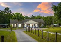 Charming brick ranch home featuring a long driveway, fenced yard, and mature trees against a colorful sky at 6901 W Dormany Rd, Plant City, FL 33565