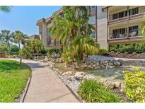 Beautiful condo exterior featuring a lushly landscaped water feature with palm trees and a sidewalk on a sunny day at 3035 Countryside Blvd # 15B, Clearwater, FL 33761