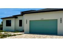 Modern home featuring a teal garage door, light stucco and a patterned brick driveway at 3339 Elkcam Blvd, Port Charlotte, FL 33952