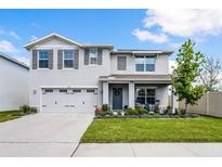 Charming two-story home featuring a well-manicured lawn, gray shutters, covered porch, and two-car garage at 1220 Tahitian Sunrise Dr, Plant City, FL 33565