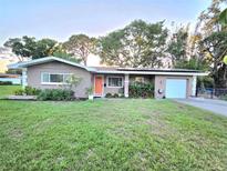 Charming one-story home with a well-manicured lawn, an orange front door, and lush landscaping at 663 68Th S Ave, St Petersburg, FL 33705