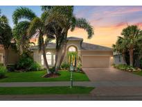 Charming single Gathering home featuring lush landscaping, manicured lawn, and a brick paver driveway at sunset at 13064 N Marsh Dr, Port Charlotte, FL 33953