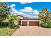 Charming home featuring a barrel tile roof, well-manicured landscaping, and a brick paver driveway leading to a three-car garage at 12784 Burns Dr, Odessa, FL 33556