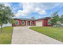 Elegant red home featuring a paver driveway, lush lawn, arched windows, and an attached two-car garage at 3244 55Th Ave N, St Petersburg, FL 33714