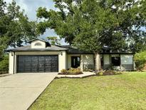 Charming single-story home featuring a black garage door, well-maintained lawn, and mature landscaping at 19543 Midway Blvd, Port Charlotte, FL 33948