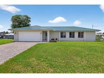 Charming single-story home featuring a green metal roof, brick driveway, and well-manicured lawn at 24277 Treasure Island Blvd, Punta Gorda, FL 33955