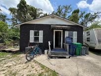 View of the home's front exterior featuring a concrete porch, black textured walls, and two shuttered windows at 3613 Deleuil Ave, Tampa, FL 33610