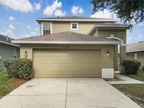 Beige two-story home featuring an attached two-car garage and manicured front bushes under a cloudy blue sky at 10429 Avelar Ridge Dr, Riverview, FL 33578