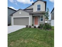 Two-story home featuring a landscaped yard, a gray garage door, and a charming peach-colored front door at 13707 Newbridge St, Spring Hill, FL 34609