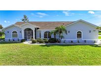 Charming single-story home with lush lawn, manicured shrubs, and welcoming screened entryway, and decorative windows at 142 Broadmoor Ln, Rotonda West, FL 33947