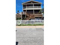 Charming multi-level home featuring multiple decks, brown siding, and a quaint white picket fence at 19105 Whispering Pines Dr, Indian Shores, FL 33785