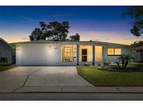 Charming single-story home with a manicured lawn, stucco exterior, and attached garage at dusk at 3410 Allandale Dr, Holiday, FL 34691