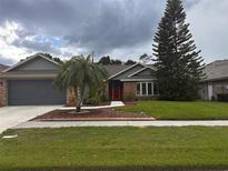Charming single-Gathering home featuring a red door, well-manicured lawn, and mature trees under a cloudy sky at 1403 Ventana Dr, Sun City Center, FL 33573