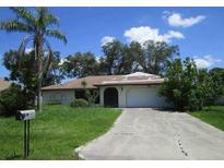 Single-story home with a palm tree and a driveway leading to an attached two-car garage at 13382 Drummond Ave, Port Charlotte, FL 33953