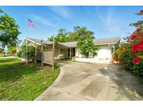 Charming single-story home featuring a covered carport, lush landscaping, and a flagpole with the American flag at 5728 Colonial Dr, New Port Richey, FL 34653