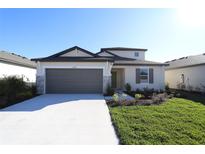 Charming single-story home featuring a manicured lawn, neutral paint, and a two-car garage with stone accents at 9868 Last Light Gln, Parrish, FL 34219