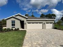 Charming single-story home featuring a three-car garage, a beautiful stone driveway, and lush landscaping at 9049 Players Dr, Weeki Wachee, FL 34613