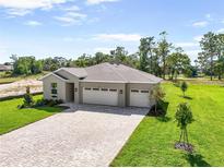 Beautiful single-story home featuring a three-car garage, neutral paint, and a brick paver driveway on a sunny day at 9049 Players Dr, Weeki Wachee, FL 34613