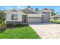 Charming single-story home featuring a manicured lawn, brick driveway, stone accents, and a two-car garage at 9093 Players Dr, Weeki Wachee, FL 34613
