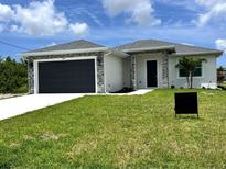 Charming single-story home showcasing a lush lawn, complemented by a sleek, dark garage door and stone accents at 183 Wright Drive, Rotonda West, FL 33947