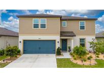 Two-story home featuring a blue garage door, tan siding, and a well-manicured front yard at 3884 Capri Coast Dr, Plant City, FL 33565