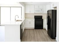 Bright kitchen features white cabinets, quartz counters, stainless sink and black appliances at 7314 Patio Row, Hudson, FL 34667