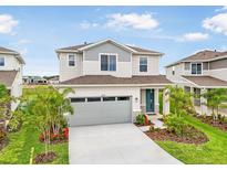 Two-story home showcasing a two-car garage, blue front door, well-manicured lawn, and vibrant landscaping at 6058 Jensen View Ave, Apollo Beach, FL 33572
