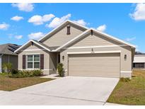 Charming single-Gathering home featuring neutral paint, a two-car garage, and a well-manicured front lawn on a sunny day at 16750 Sunburst Lake St, Wimauma, FL 33598