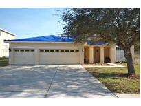 Beige two-story house with a three-car garage and mature trees at 4909 Larkenheath Dr, Spring Hill, FL 34609