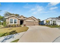 Tan three-car garage home with landscaping at 14069 Wineberry Dr, Dade City, FL 33525