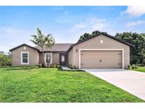 Tan one-story house with a two-car garage and lush lawn at 12461 Patsy Ave, Port Charlotte, FL 33981