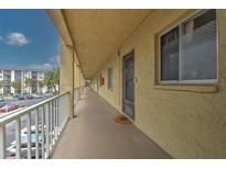 A long, covered hallway with yellow walls leading to apartments, and a view of a parking lot and building to the side at 3753 Lake Bayshore Dr # H305, Bradenton, FL 34205