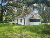 White house exterior with screened porch, surrounded by lush green grass and mature trees at 1205 S Main St, Brooksville, FL 34601