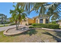 Charming yellow home featuring a well-manicured lawn with palm trees and meticulously landscaped flowerbeds at 1007 Emerald Dunes Dr, Sun City Center, FL 33573