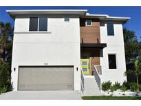 Modern two-story home with a yellow front door, a two-car garage, and a combination of white and wood-paneled siding at 7615 S Swoope St, Tampa, FL 33616