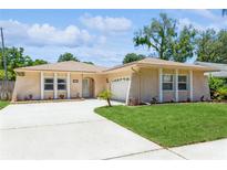 Tan house with white trim, attached garage, and landscaped lawn at 2476 Grove Ridge Dr, Palm Harbor, FL 34683