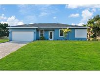 Single-story home with a blue exterior, white garage door and a manicured lawn at 18400 Tulane Ave, Port Charlotte, FL 33954