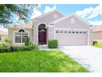 Tan house with purple door, two-car garage, and green lawn at 3524 Beaumont Loop, Spring Hill, FL 34609