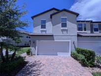 Two-story townhome with gray siding, a white garage door, and a brick paved driveway at 10066 Corso Milano Dr, Tampa, FL 33625