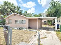 Charming single-story home with a covered carport, framed by lush trees and secured by a chain-link fence at 8312 N Mulberry St, Tampa, FL 33604
