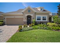 Tan house with a stone facade, two-car garage, and manicured landscaping at 13939 Swallow Hill Dr, Lithia, FL 33547