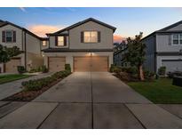 Two-story house with a tan facade, two-car garage, and landscaping at 5184 Sylvester Loop, Tampa, FL 33610