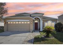 Tan house with red door, two car garage, and landscaped yard at 7720 Rathdown Ln, Wesley Chapel, FL 33545