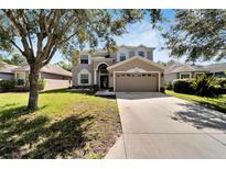 Two-story house with tan siding, large driveway, and landscaped yard at 13951 Caden Glen Dr, Hudson, FL 34669