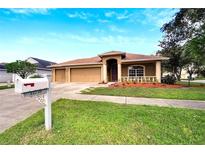 Tan three-car garage home with a red door and nicely landscaped yard at 12739 Standbridge Dr, Riverview, FL 33579